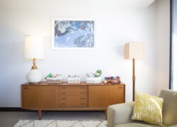 Picture of a dresser with a lamp and toys on it with a painting on the wall