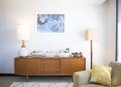 Picture of a dresser with a lamp and toys on it with a painting on the wall