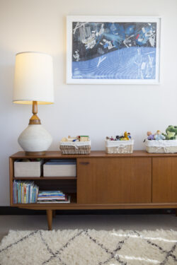 Picture of a dresser with a lamp and toys on it with a painting on the wall